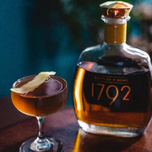 Load image into Gallery viewer, Bottle of 1792 bourbon and a cocktail with a lemon twist on a wooden surface.