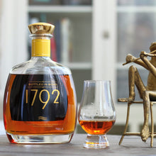 Load image into Gallery viewer, Bottle of 1792 bourbon with a glass of whiskey on a table, accompanied by a decorative figure.