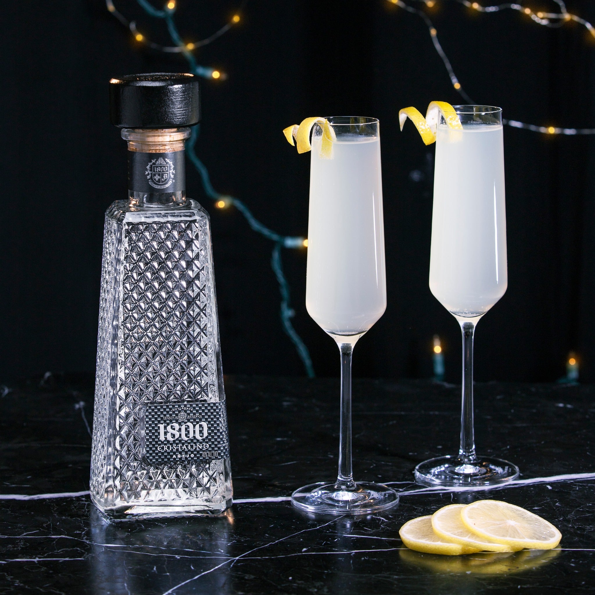 Load image into Gallery viewer, Bottle of 1800 Cristalino Añejo Jose Cuervo Tequila with two cocktails garnished with lemon slices on a dark surface.