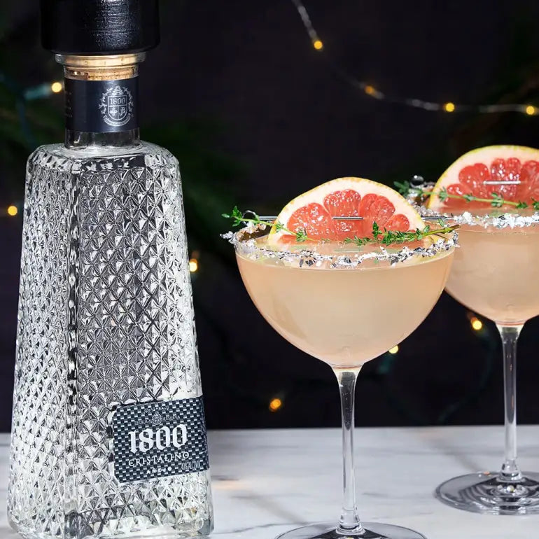 Load image into Gallery viewer, 1800 Cristalino Añejo Jose Cuervo Tequila bottle with two cocktails garnished with grapefruit on a dark background