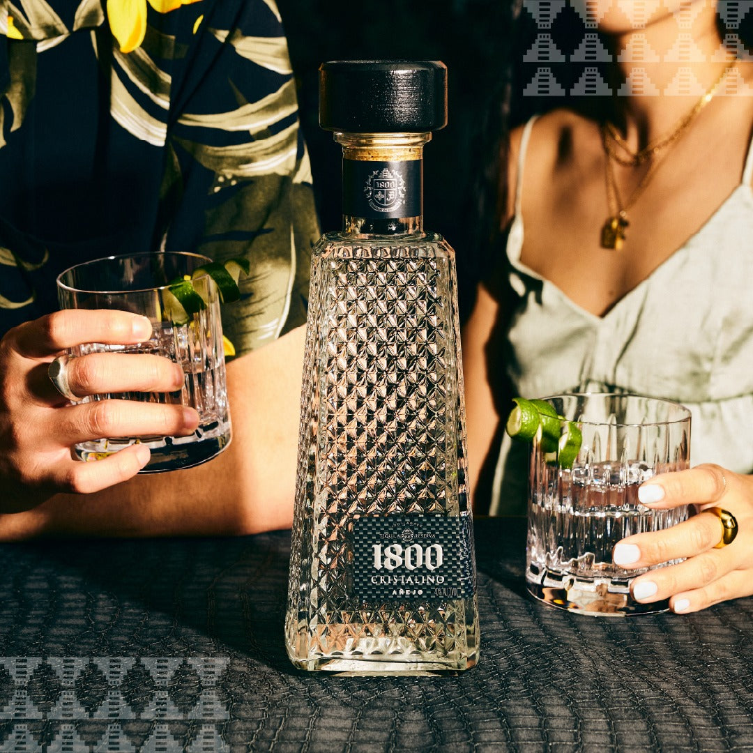Load image into Gallery viewer, 1800 Cristalino Añejo Jose Cuervo Tequila bottle with two people holding glasses in a social setting