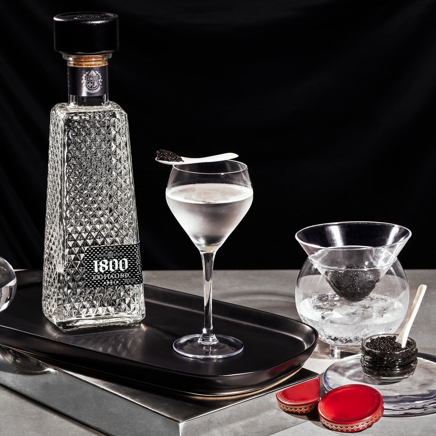 Load image into Gallery viewer, 1800 Cristalino Añejo Jose Cuervo Tequila bottle with a glass of tequila on a tray against a black background