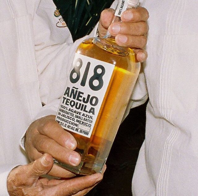 Person holding a bottle of 818 Aénjo Tequila with a white label.
