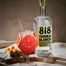 Load image into Gallery viewer, Bottle of 818 Tequila Blanco with a cocktail garnished with orange and grapefruit on a textured surface.