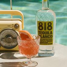 Load image into Gallery viewer, Bottle of 818 Tequila Blanco with a cocktail and orange slice by a pool.