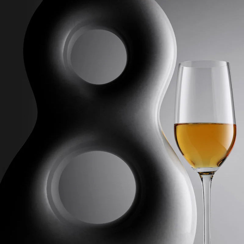 A tequila tasting glass with tequila inside next to a bottle of 818 Eight Reserve Anejo Tequila on a gray background