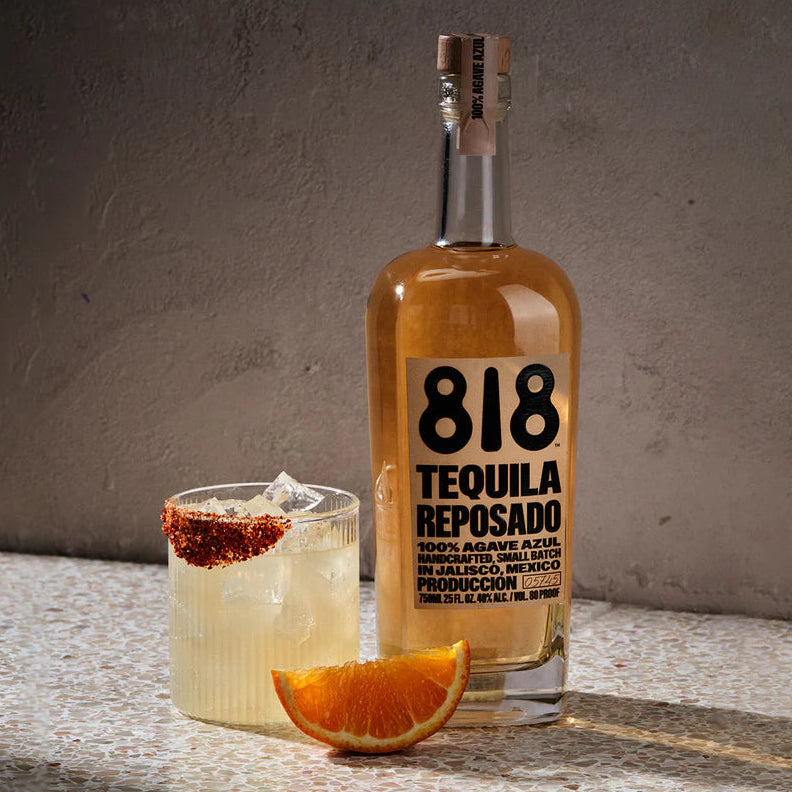 818 Tequila Reposado bottle with a cocktail and orange wedge on a textured surface.