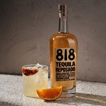 Load image into Gallery viewer, 818 Tequila Reposado bottle with a cocktail and orange wedge on a textured surface.