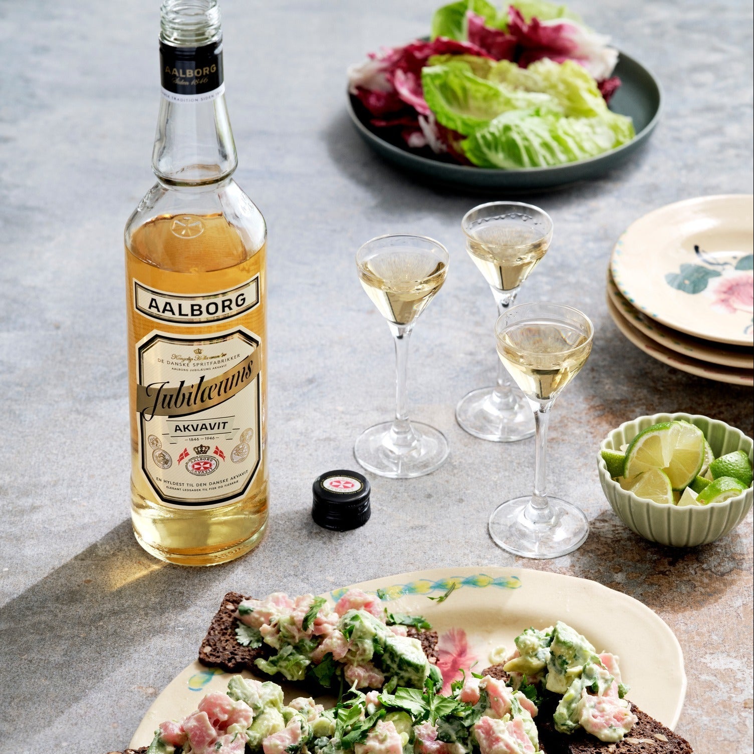 Load image into Gallery viewer, Aalborg Jubileum akvavit bottle with glasses of liquid on a table with food.