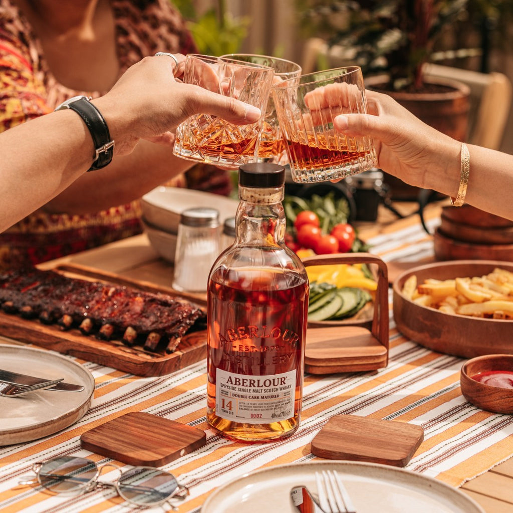 Two people toasting with Aberlour 14 year old whisky at a dining table with food and drinks.