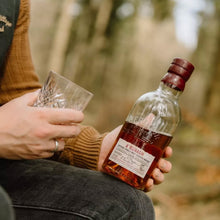 Load image into Gallery viewer, Person holding a bottle and glass of Aberlour Abunadh whisky in a forest setting