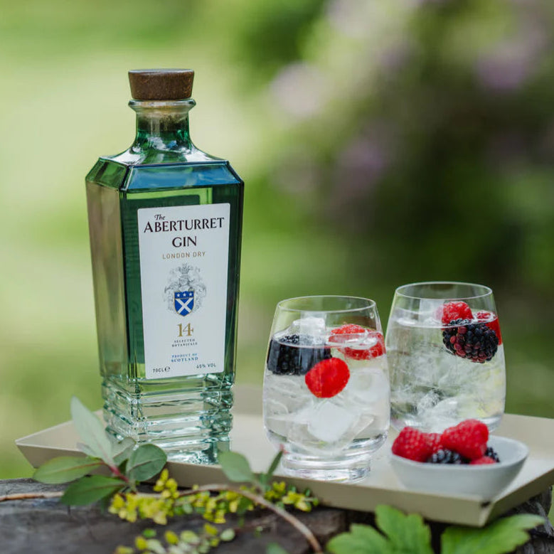 Load image into Gallery viewer, A bottle of Aberturret London Dry Gin stands on a tray beside two glasses filled with ice and berries, set outdoors on a wooden surface with a blurred green garden background.