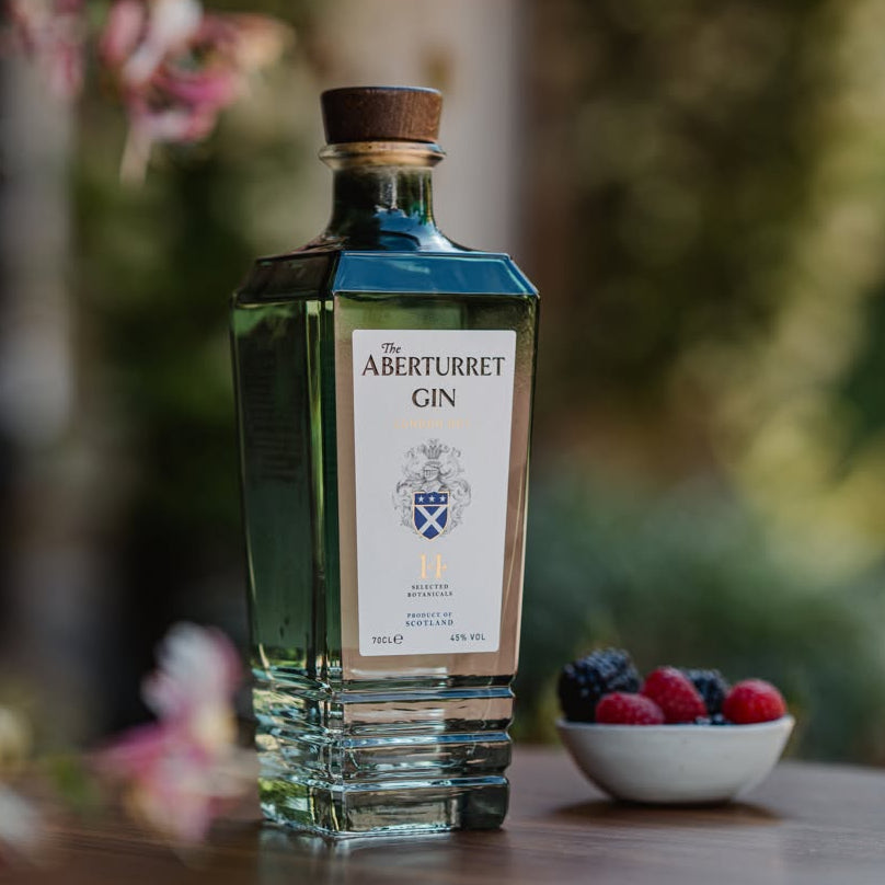 Load image into Gallery viewer, A bottle of Aberturret London Dry Gin on a wooden table, with a small bowl of fresh berries in the background, set against a blurred outdoor garden environment.