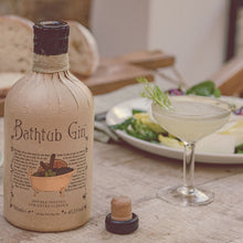 Load image into Gallery viewer, Bottle of Bathtub Gin on a table with a cocktail and food in the background