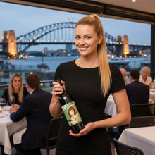 Load image into Gallery viewer, Woman holding a bottle of Adelina Wines Grenache wine with a Sydney Harbour Bridge view in the background