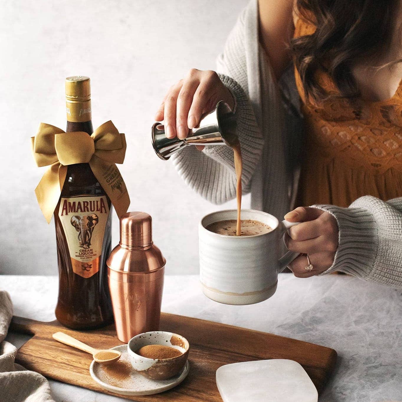 Load image into Gallery viewer, A bottle of Amarula Cream Liqueur that has a golden bow around it in the background a woman pouring amarula into a cup