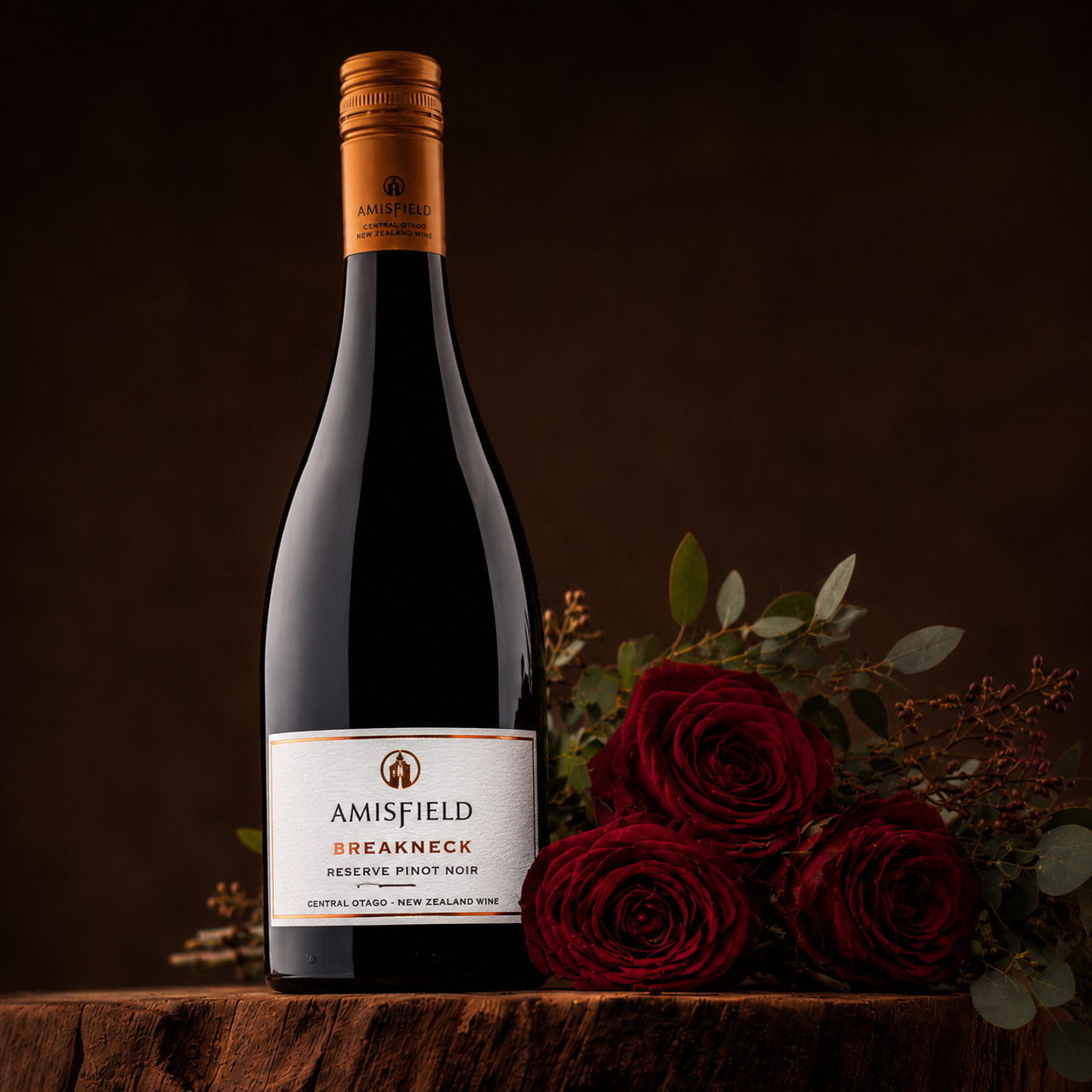 Load image into Gallery viewer, A bottle of Amisfield Breakneck Reserve Pinot Noir red wine stands on a wooden surface next to three red roses and greenery, against a dark brown background.