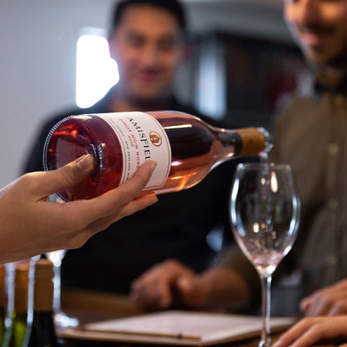 Load image into Gallery viewer, Person pouring Amisfield rose wine into a glass with two blurred people in the background.