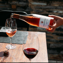 Load image into Gallery viewer, A person pouring a glass of Amisfield Rosé to a glass thats standing on a wooden table and with a brick background