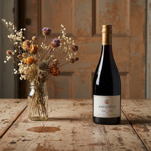 Load image into Gallery viewer, Bottle of Amisfield Pinot Noir wine on a wooden table with a vase of flowers.
