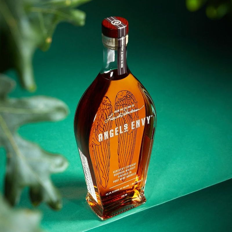 Bottle of Angels Envy bourbon on a green background with leaves.