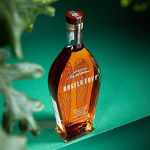 Load image into Gallery viewer, Bottle of Angels Envy bourbon on a green background with leaves.