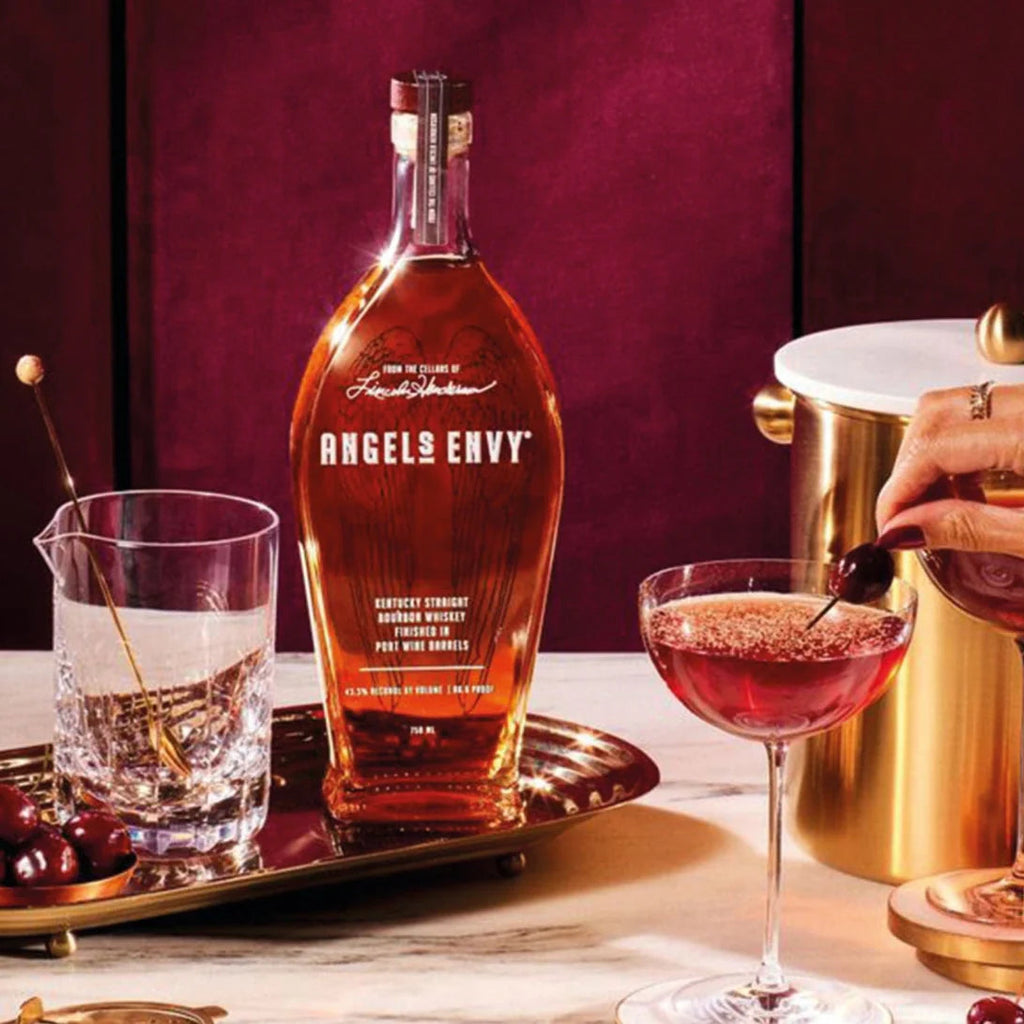 Bottle of Angels Envy bourbon with a cocktail glass and cherry on a table.
