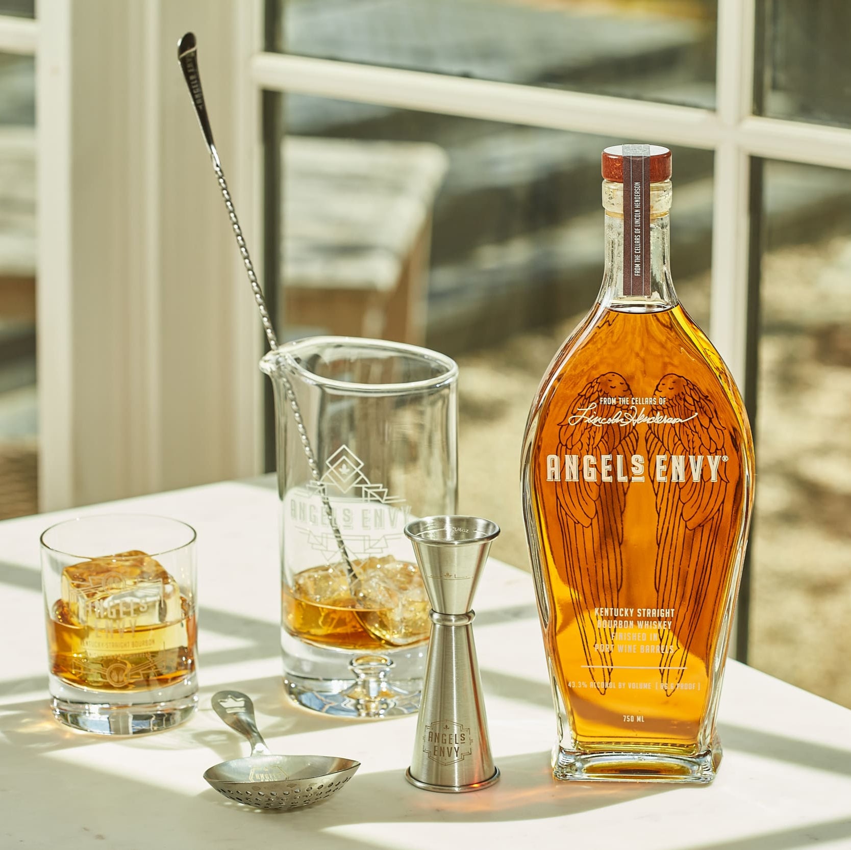Load image into Gallery viewer, Angel &amp; Envy bourbon bottle with glasses and bar tools on a table.