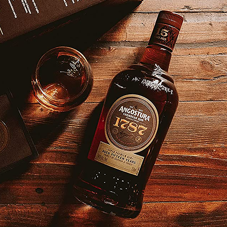 Angostura 1787 rum bottle on a wooden surface with a glass of rum.