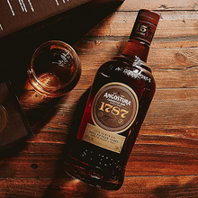 Load image into Gallery viewer, Angostura 1787 rum bottle on a wooden surface with a glass of rum.