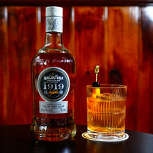 Load image into Gallery viewer, Bottle of Angostura 1919 rum with a cocktail in a glass on a wooden surface.
