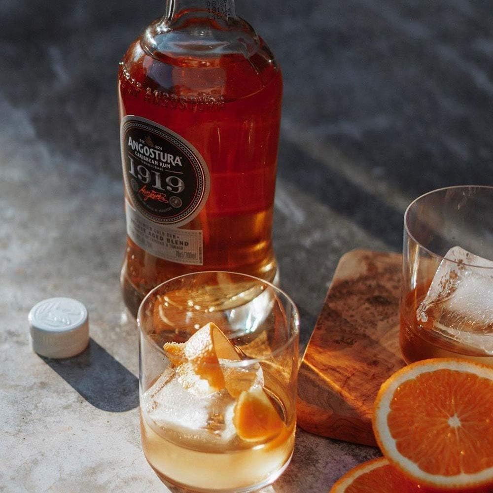 Angostura 1919 bottle with two glasses of cocktail and orange slices on a stone surface