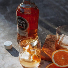 Load image into Gallery viewer, Angostura 1919 bottle with two glasses of cocktail and orange slices on a stone surface