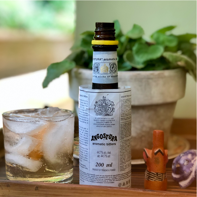 Load image into Gallery viewer, Angostura aromatic bitters bottle with a glass of iced drink on a wooden surface.