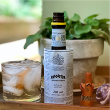 Load image into Gallery viewer, Angostura aromatic bitters bottle with a glass of iced drink on a wooden surface.