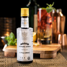 Load image into Gallery viewer, Bottle of Angostura aromatic bitters with a cocktail in the background