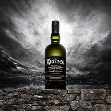 Load image into Gallery viewer, Ardbeg 10 year old whisky bottle on a stone wall with a dramatic sky background