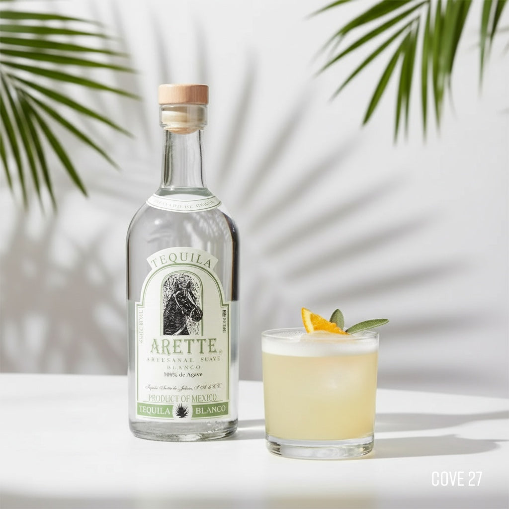 Load image into Gallery viewer, Arette Artesanal Suave Blanco tequila bottle with a cocktail on a white surface with palm leaves in the background