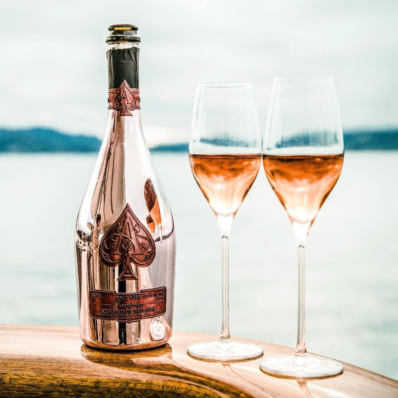 Load image into Gallery viewer, A bottle of Armand de Brignac Ace of Spades Rosé Champagne with two champagne flutes next to it with a sea view in the background.