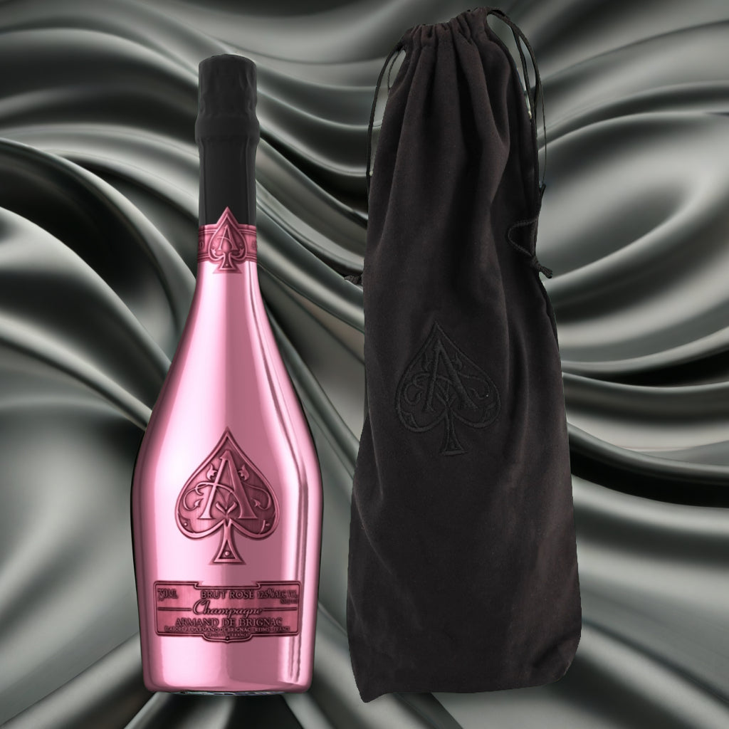 Load image into Gallery viewer, A metallic pink bottle of Armand de Brignac Ace of Spades Rosé champagne with an embossed black spade symbol and a black neck wrap, shown next to a black drawstring pouch with a matching embossed spade, set against a dark grey satin fabric background.