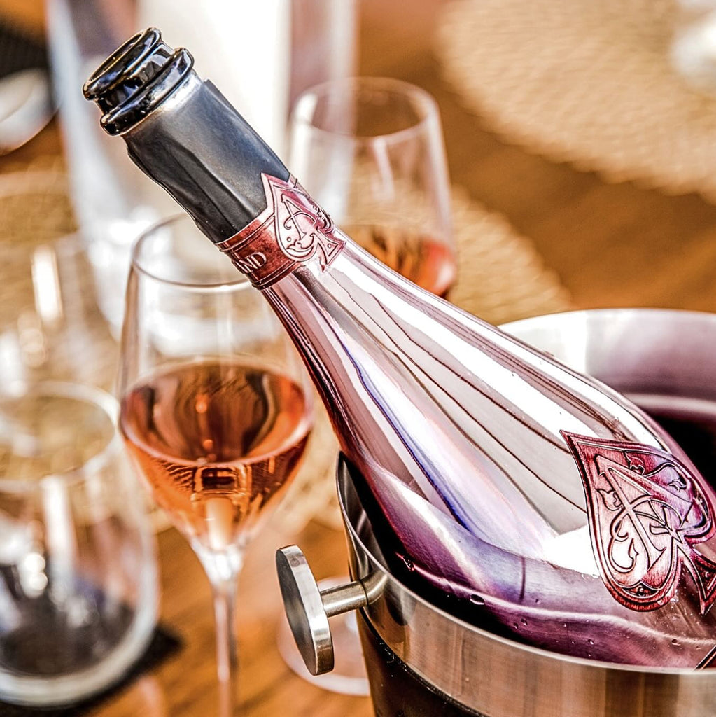 A bottle of champagne in a pink bottle in a ice bucket n a wooden table