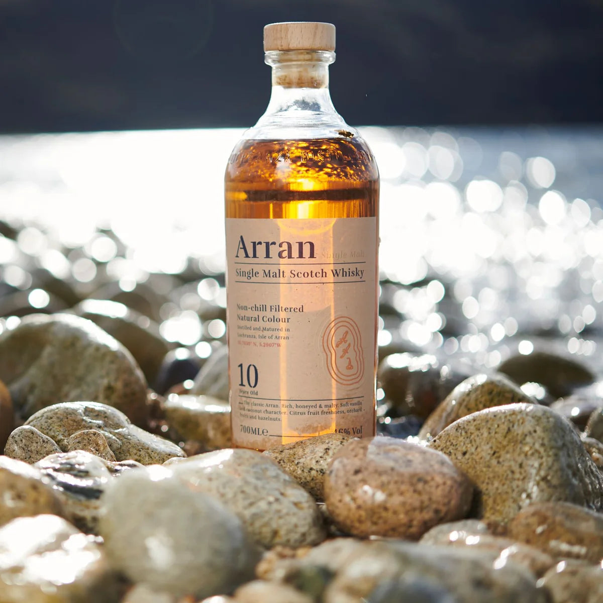 Load image into Gallery viewer, Arran 10 year old Single Malt Scotch Whisky bottle on pebbles by the water