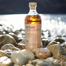 Load image into Gallery viewer, Arran 10 year old Single Malt Scotch Whisky bottle on pebbles by the water