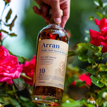 Load image into Gallery viewer, Arran 10 year old whisky bottle held by a hand with flowers in the background