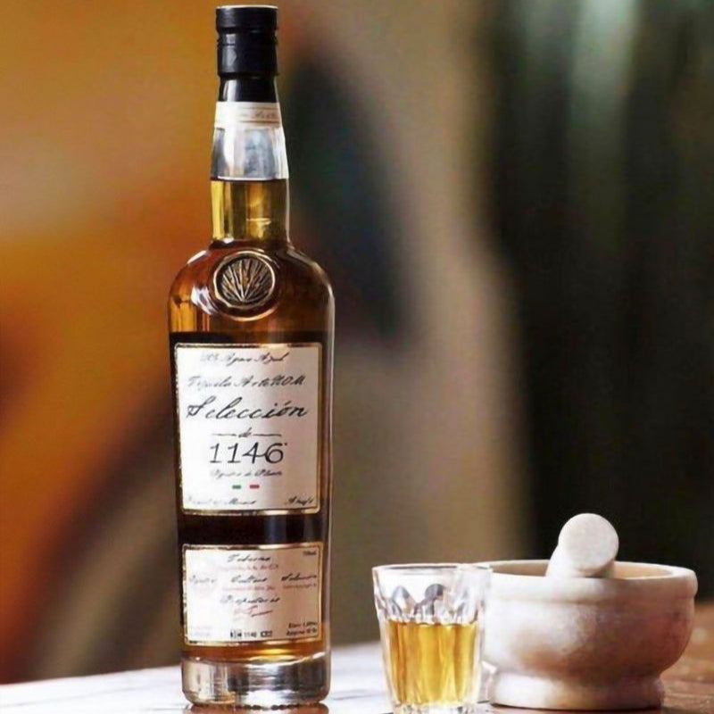 Load image into Gallery viewer, Bottle of 1146 tequila with a glass of rum on a wooden surface