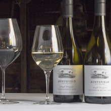 Load image into Gallery viewer, Wine bottles and glasses on a rustic wooden table with a barn-style background.