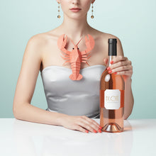 Load image into Gallery viewer, Woman holding a bottle of BY.OTT Provence Rose Magnum wine with a lobster-shaped wine glass holder on a light blue background
