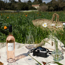 Load image into Gallery viewer, Picnic setup with wine, food, and glasses in a field under a cloudy sky.