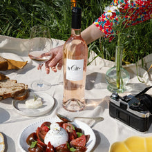 Load image into Gallery viewer, A bottle of rose wine on a pic nic blanket in the grass with some bread and cheese.