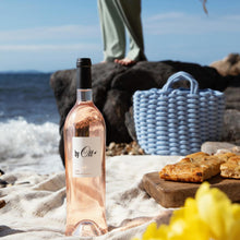 Load image into Gallery viewer, Rose wine bottle on a beach with a person and picnic setup in the background